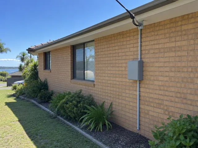 Brick house wall with overhead service cable, attachment bracket and external switchboard box in Long Jetty